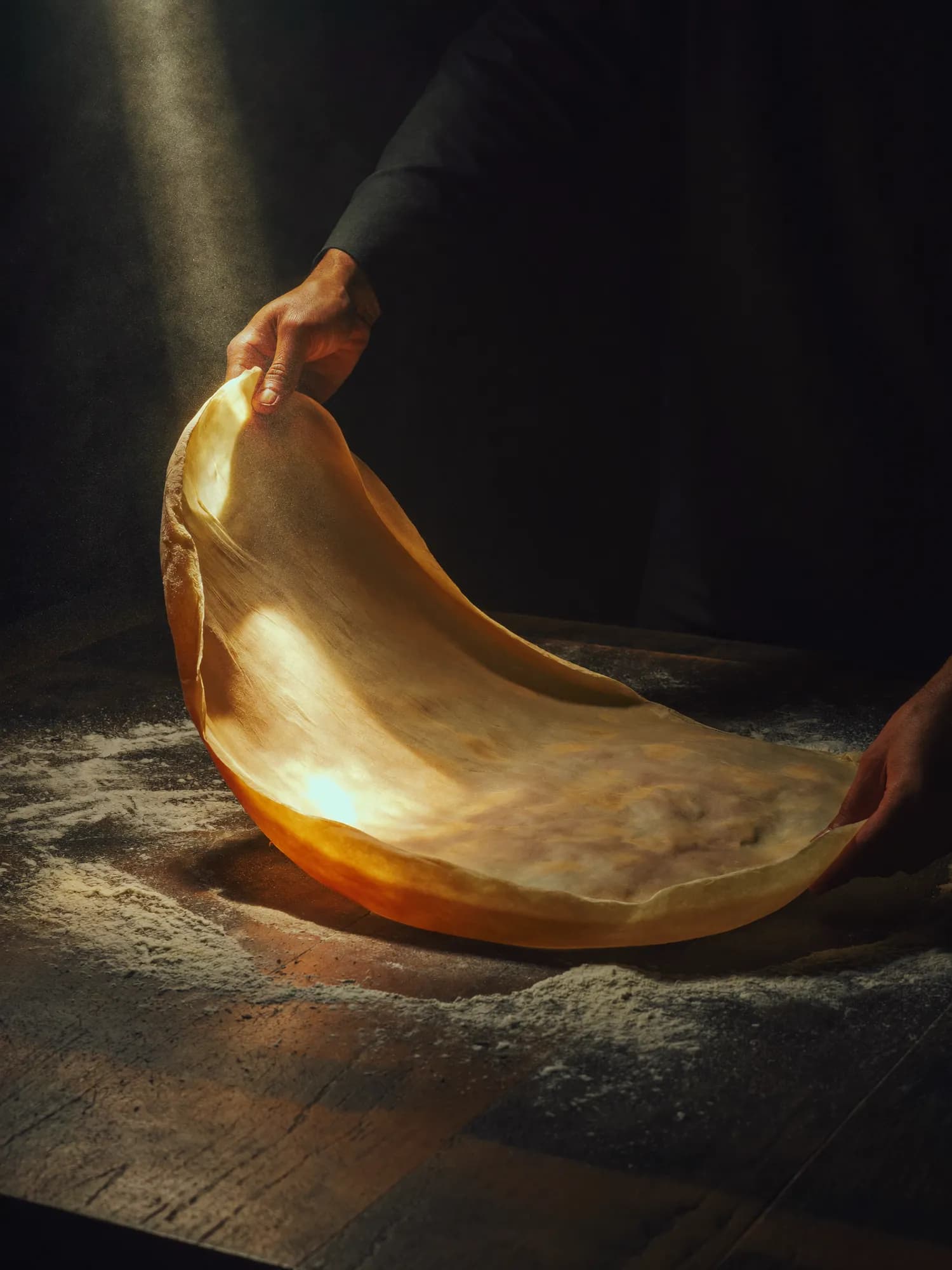 Hands stretching feteer dough into a thin, translucent sheet